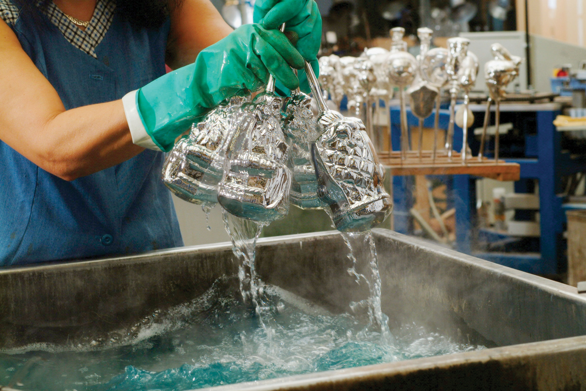 A silver sink filled with blue liquid with a person dunking glasses into the liquid.