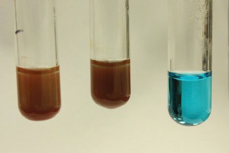 a vial on the left with a medium brown liquid in it; a vial in the middle with a dark brown liquid in it; a vial on the right with blue liquid in it